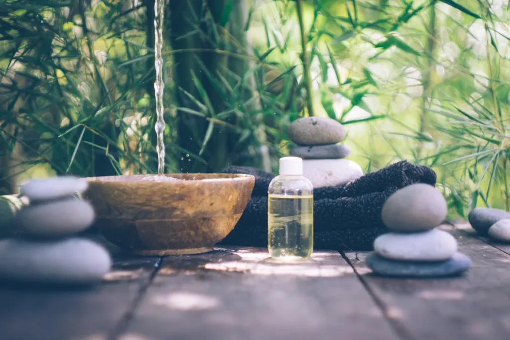 Spa essentials including stones, oil, and bowl on wooden table.